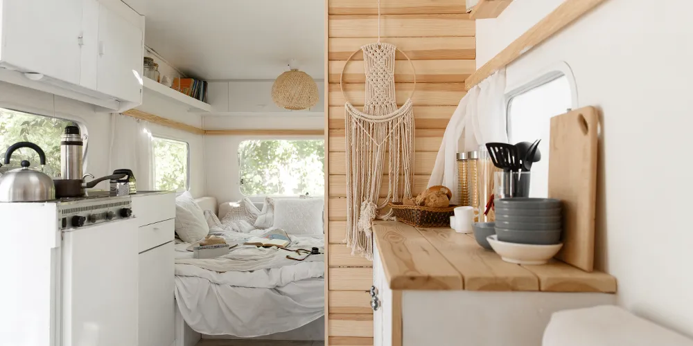 Modern caravan interior with cozy bed, kitchenette, wooden cabinetry, and boho-inspired decor, creating a welcoming and stylish living space.